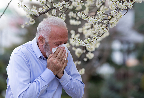 A person holding a tissue and sneezing due to spring allergies